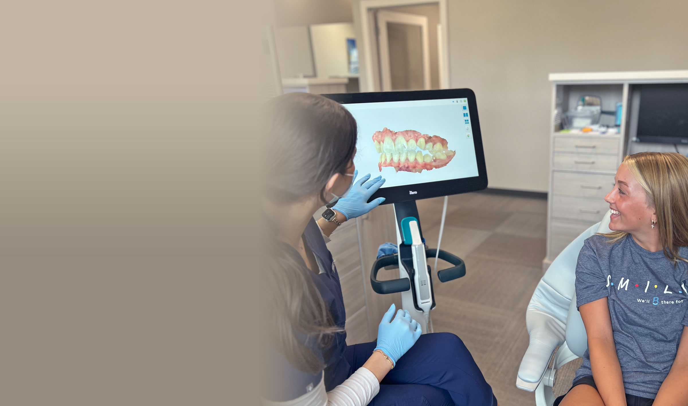 A dental professional shows a patient a 3D dental scan on a screen. The setting is a modern dental office with equipment.